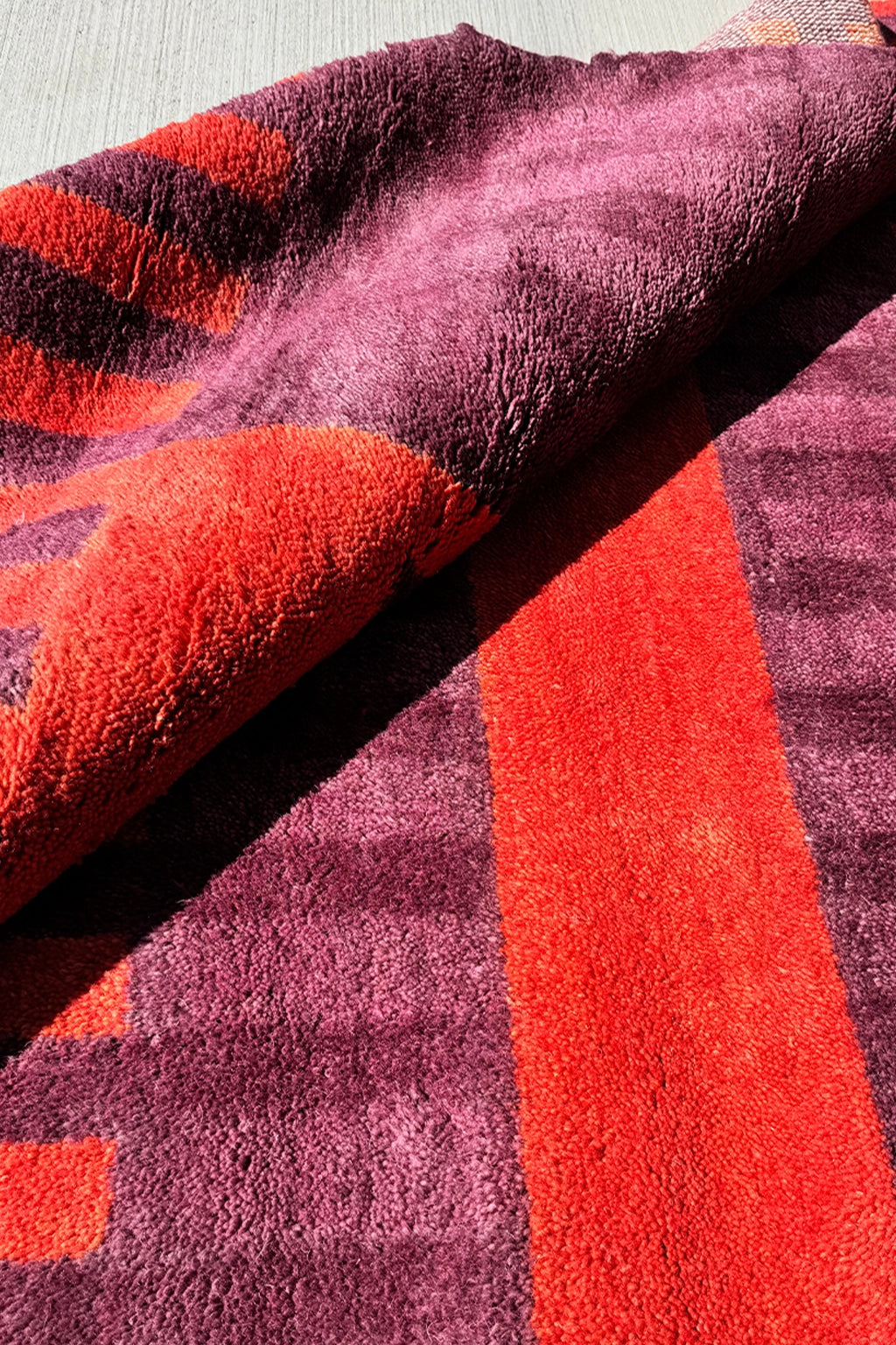 purple and red square rug folded to show pile detail