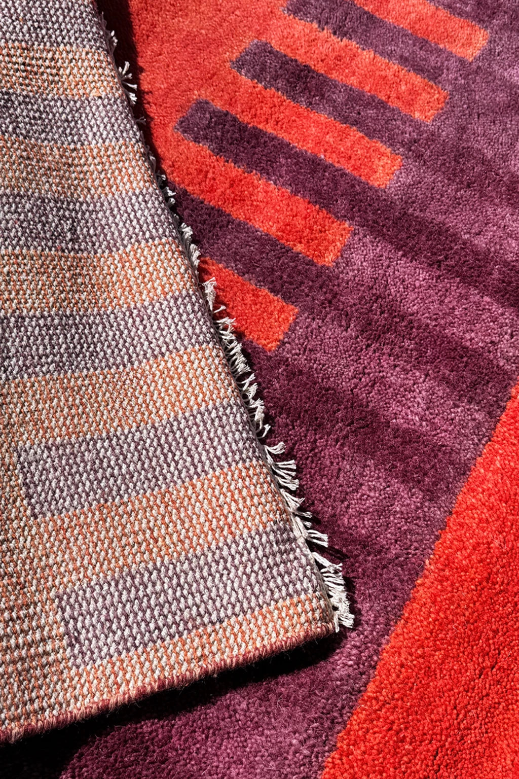 Close-up of two textured rugs with geometric patterns in red, purple, and brown.