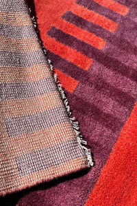Close-up of two textured rugs with geometric patterns in red, purple, and brown.