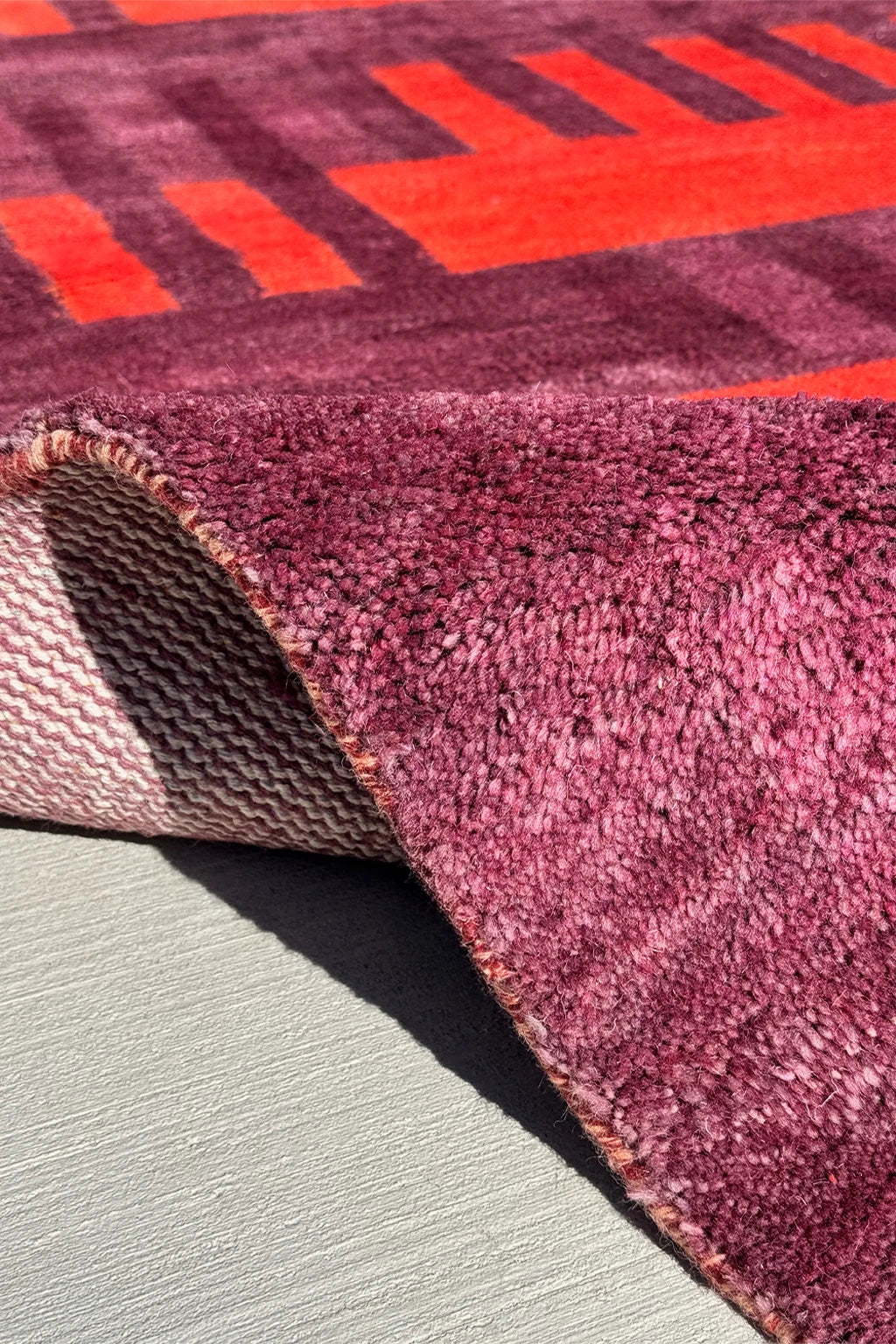 Close-up of a textured purple and red rug on a neutral surface