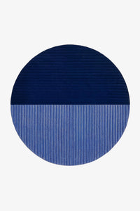 A round area rug with a split color-block design, featuring a dark navy blue top half and a medium blue bottom half, both with a ribbed texture, shown on a plain white background.