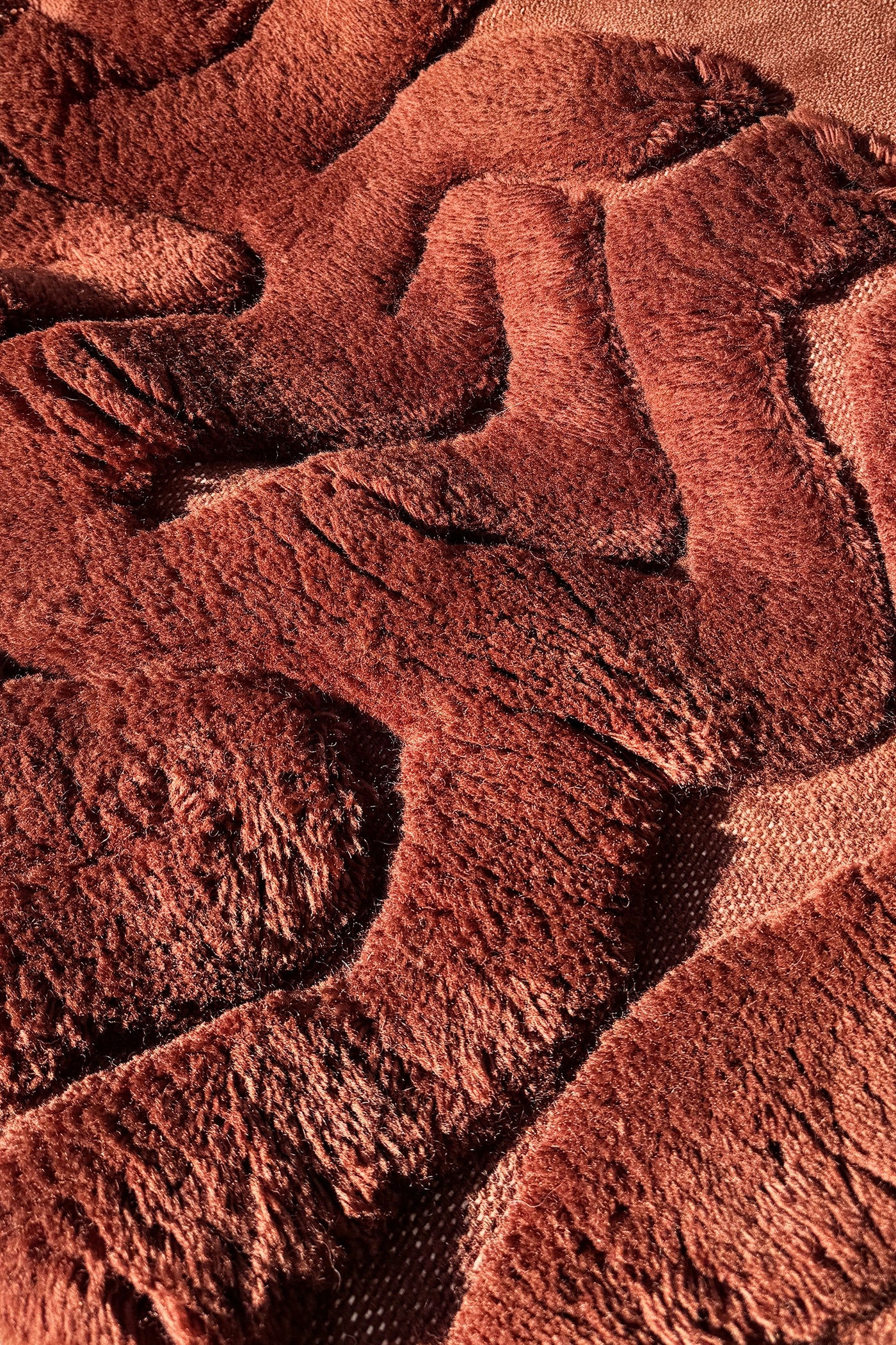 A close-up of a textured, wavy patterned runner rug in a warm reddish-brown or rust color, showing the plush, looped pile and woven backing.