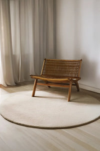 Natural cream round wool rug styled under mid-century woven chair, perfect for 6ft or 8ft round sizing lifestyle