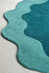Wavy edge detail of teal and turquoise abstract shaped rug, a soft wool novelty rug with a puddle-like silhouette ideal for fun modern interiors
