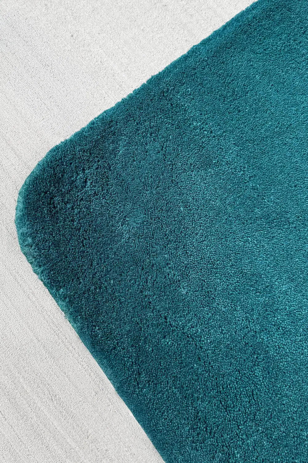 Angled view of dark teal quarter rug with soft curves and sculpted edge, ideal as a unique corner accent in contemporary rooms