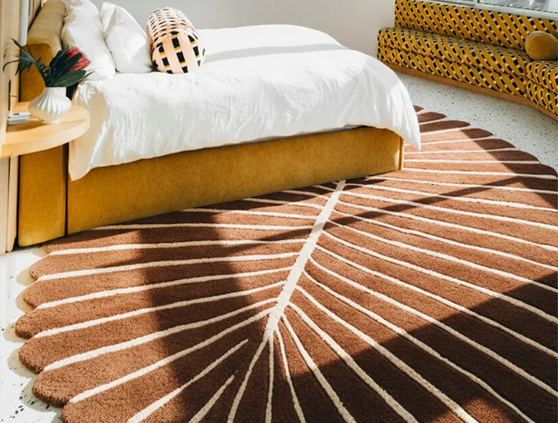 Brown and beige leaf shaped rug in a room with a bed and decorative pillows.
