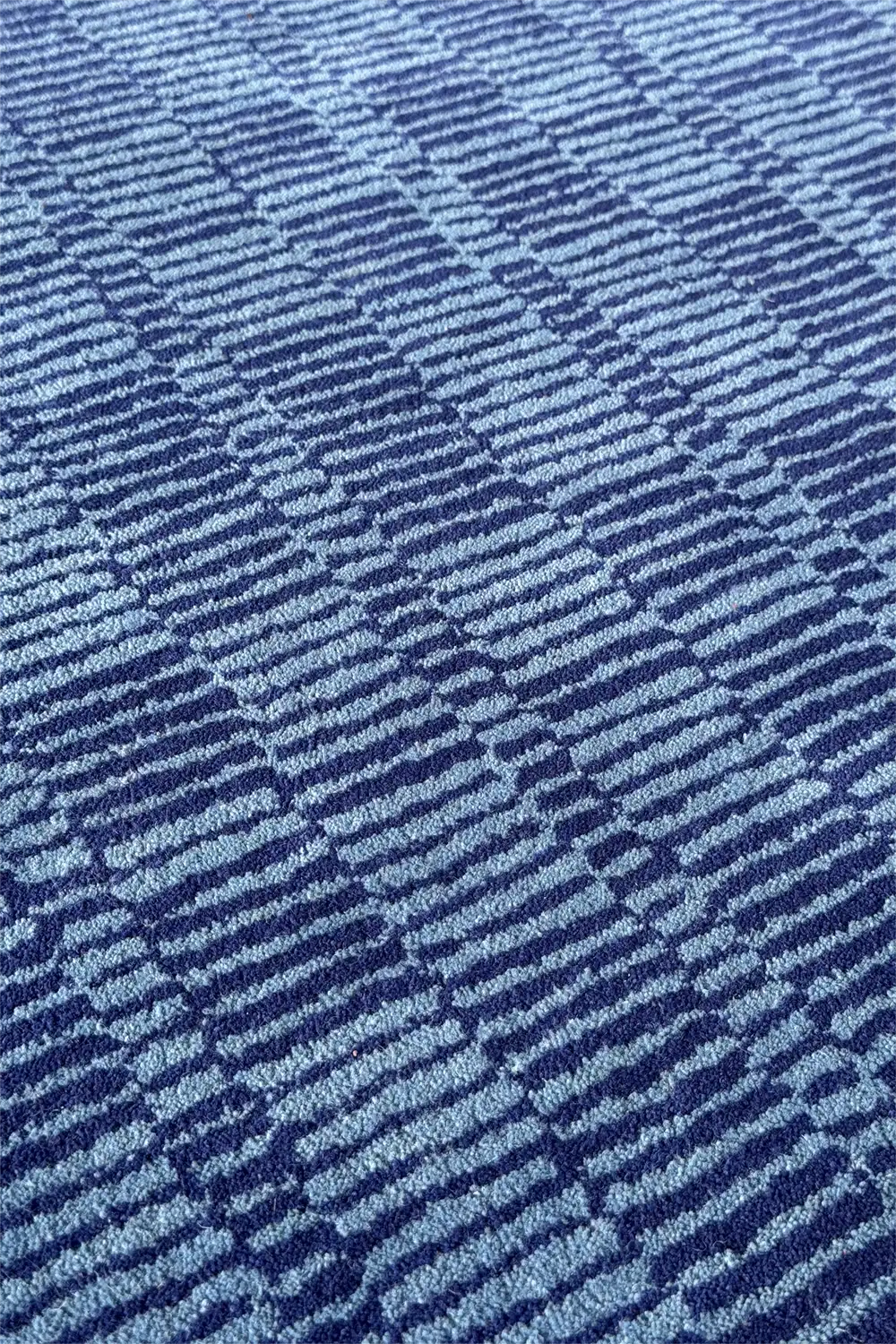 Striped and checkered wool rug in dark and light blue tones, adding texture to a navy bedroom floor