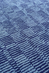 Striped and checkered wool rug in dark and light blue tones, adding texture to a navy bedroom floor