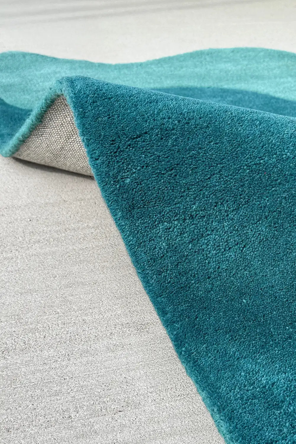 Folded edge detail revealing the back of a scalloped corner rug, showcasing thickness and curved outline in bold teal tones