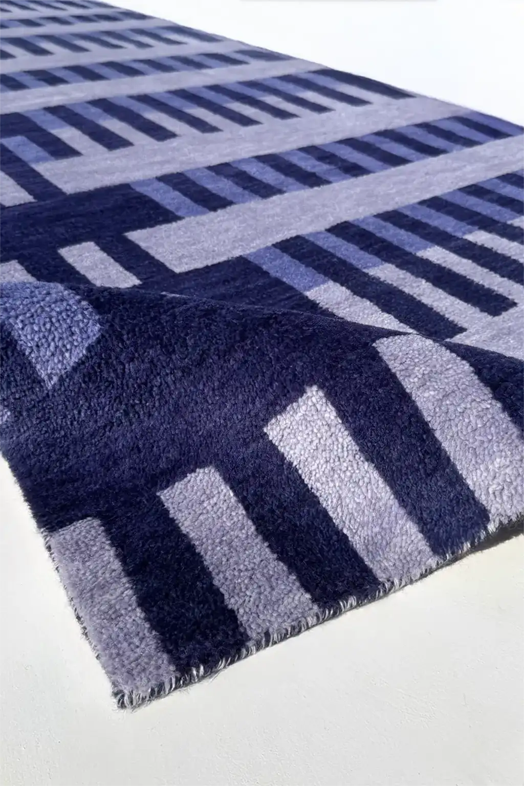 A close-up of a plush runner rug with a geometric pattern in navy blue, medium blue, and light gray, shown on a white surface.