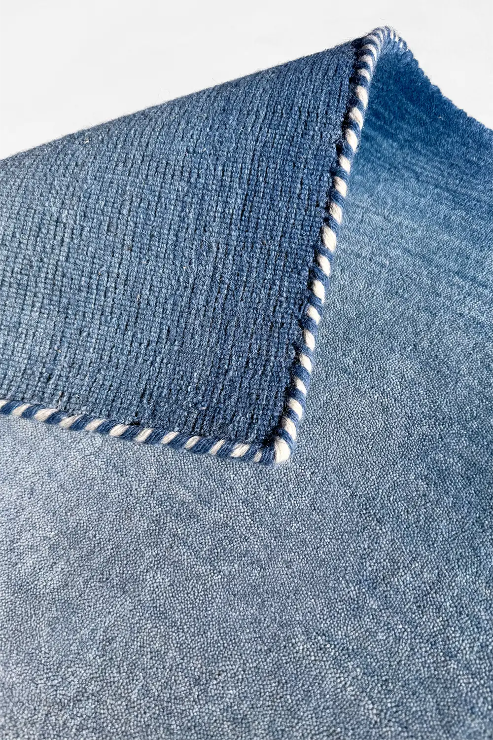 Close-up of a blue modern area rug with white trim on a light gray background
