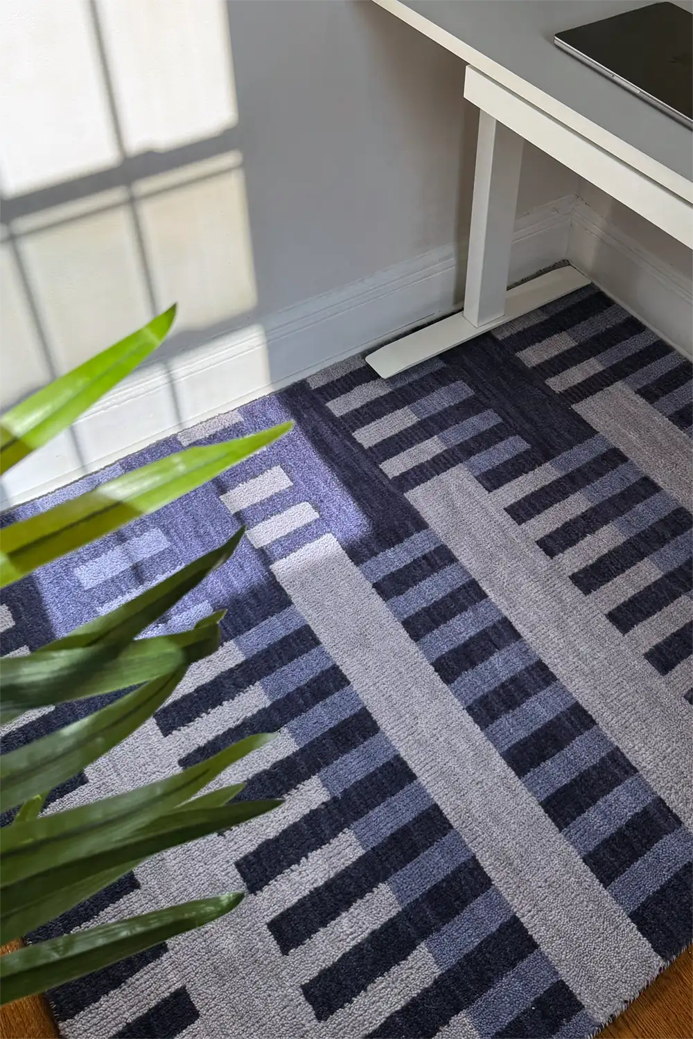 Patterned blue modern rug on a wooden floor with a plant and desk corner.