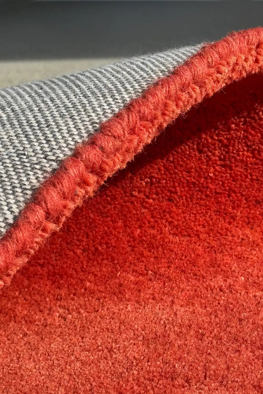 Close-up of a thick red textured rug with gray cotton backing.