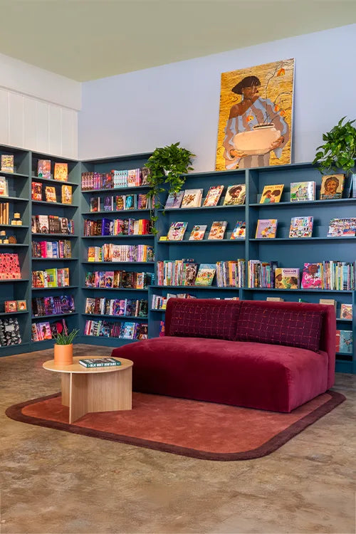 Modern interior with a red sofa, brown curved wool rug, bookshelves, and a painting on the wall.