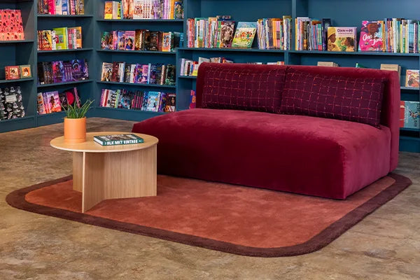 Red sofa on a modern brown rug with curved borders in a bookstore with bookshelves in the background