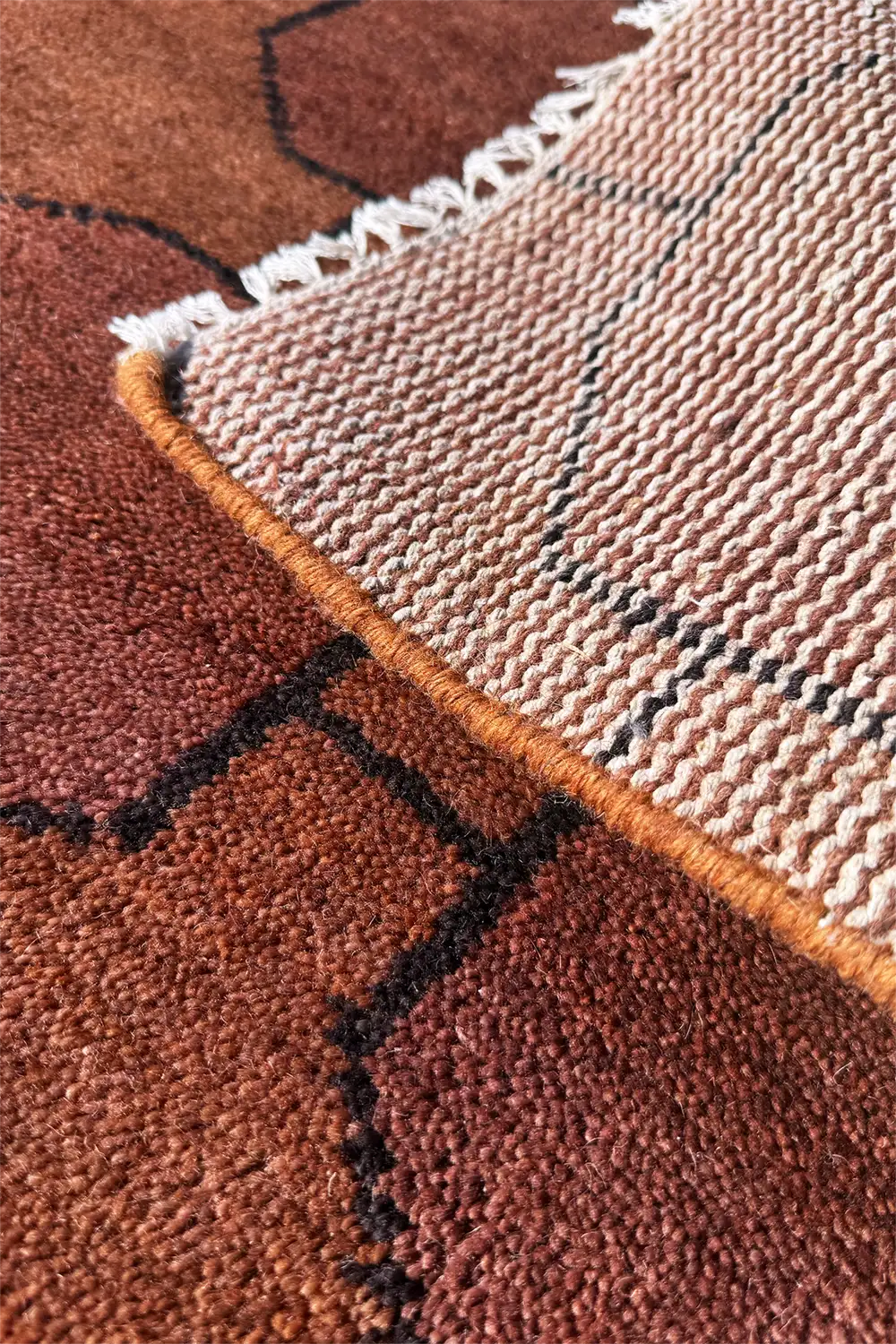 Close-up of a textured brown and rust wool rug with geometric patterns.