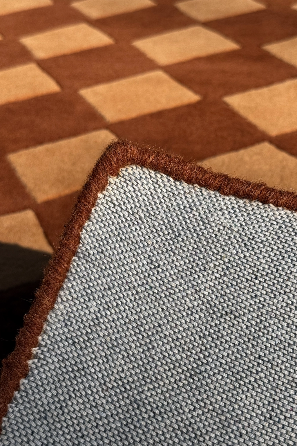 bound edge of brown wool rug hand-tufted with geometric diamond checkerboard pattern