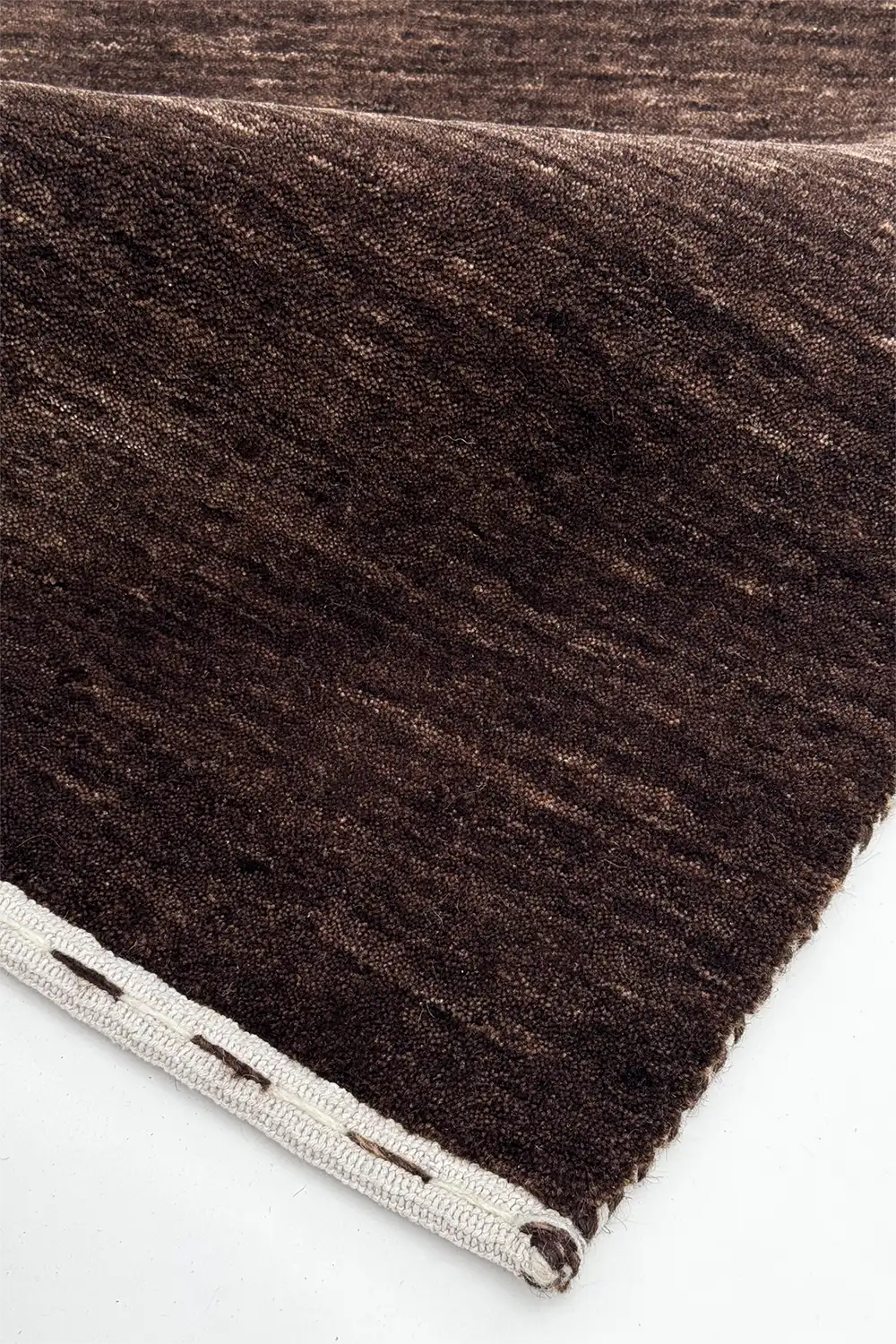 Close-up of a dark chocolate brown textured wool rug corner on a white background
