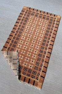 Tan and black mid-century modern runner rug laid out flat, handmade wool with bold border and square motif