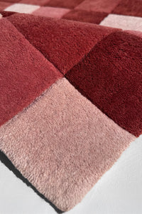 Close-up of a textured red and pink rug with geometric checkered pattern