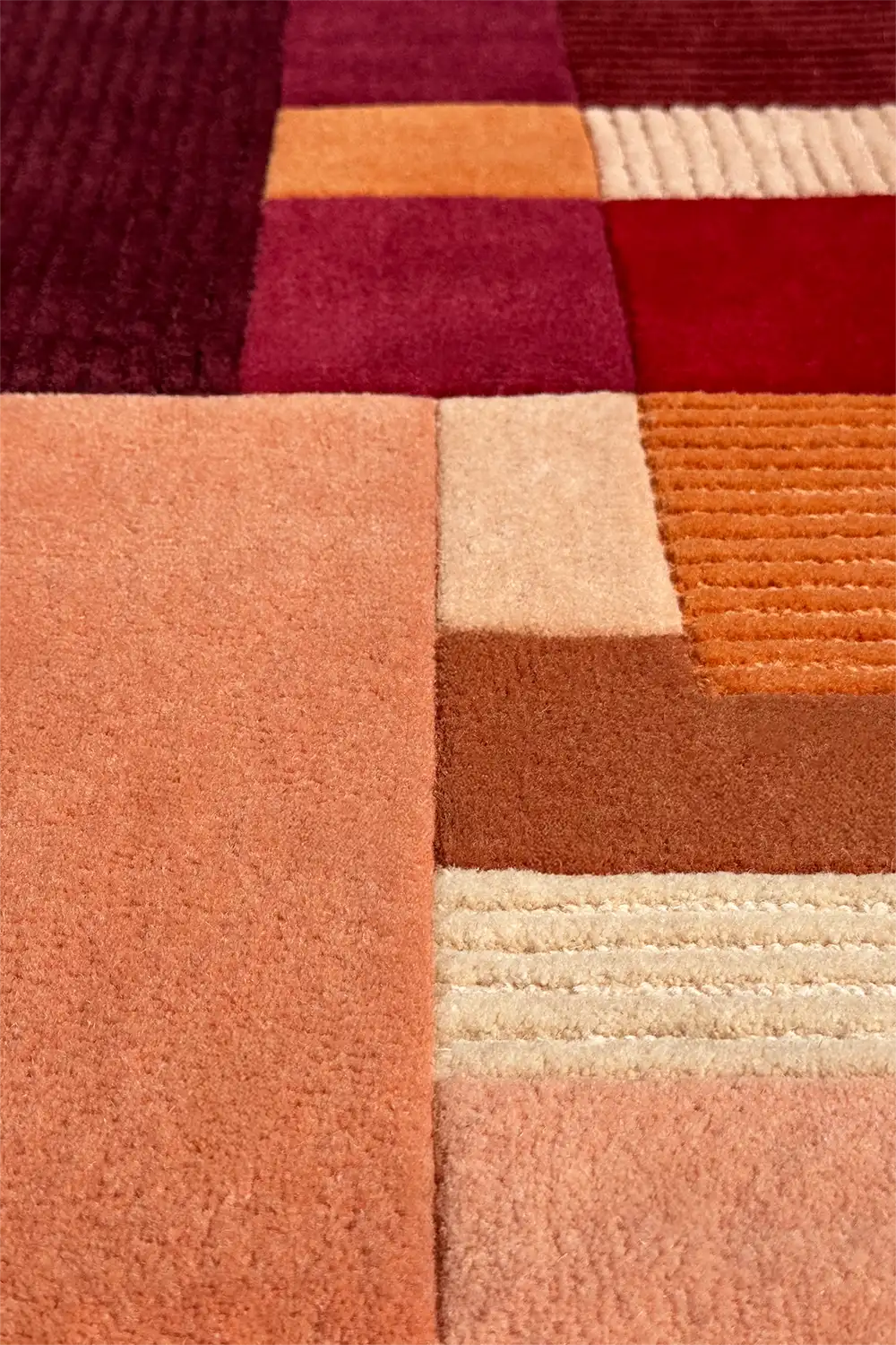 Close-up of a textured rug with geometric pattern in red, orange, and beige colors.