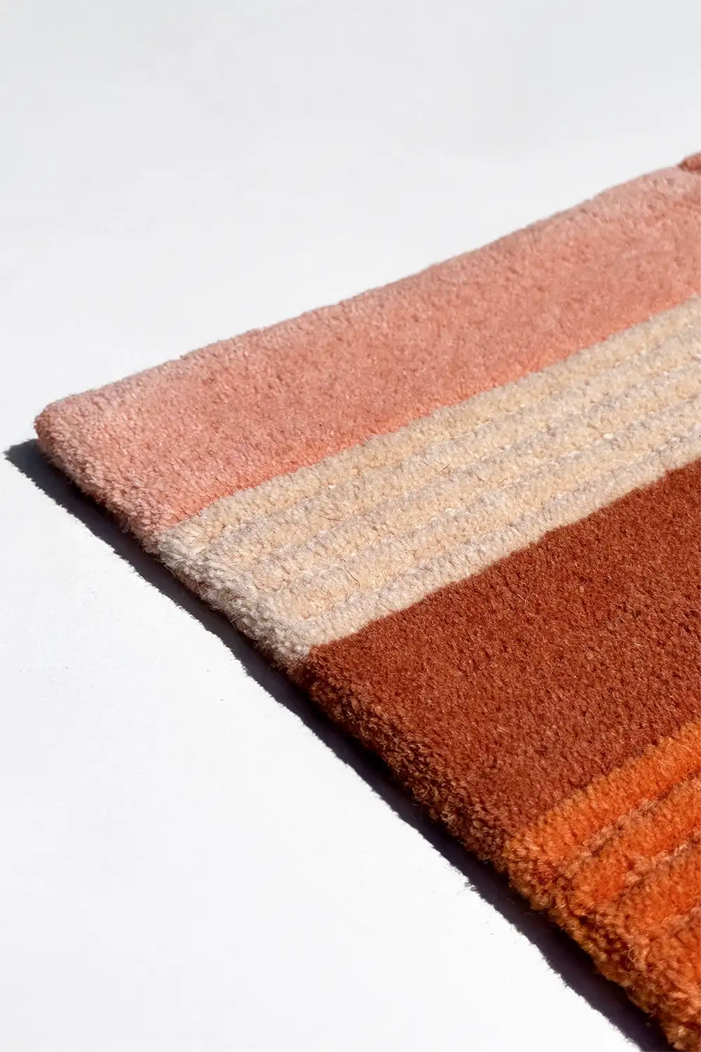 Close-up of a striped rug with pink, beige, and orange colors on a white background.
