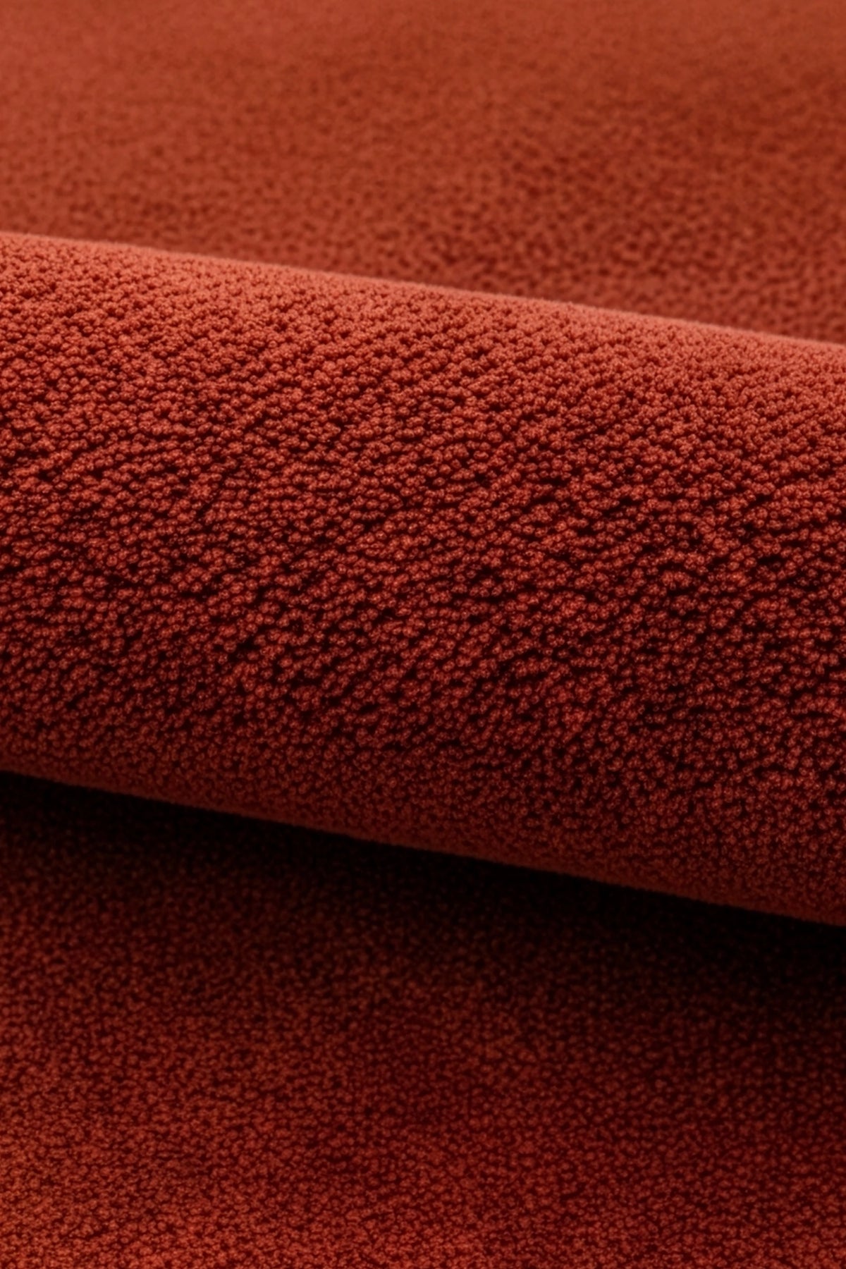 A close-up of a textured terracotta red burnt orange wool rug, showing a rolled section that highlights its soft surface texture.