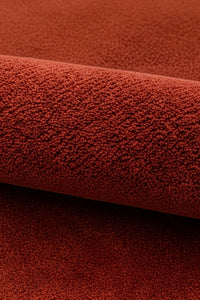 A close-up of a textured terracotta red burnt orange wool rug, showing a rolled section that highlights its soft surface texture.