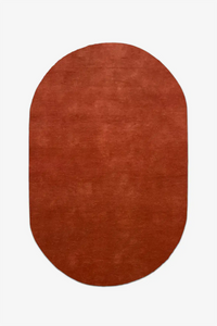 Oval-shaped burnt orange red rug on a white background