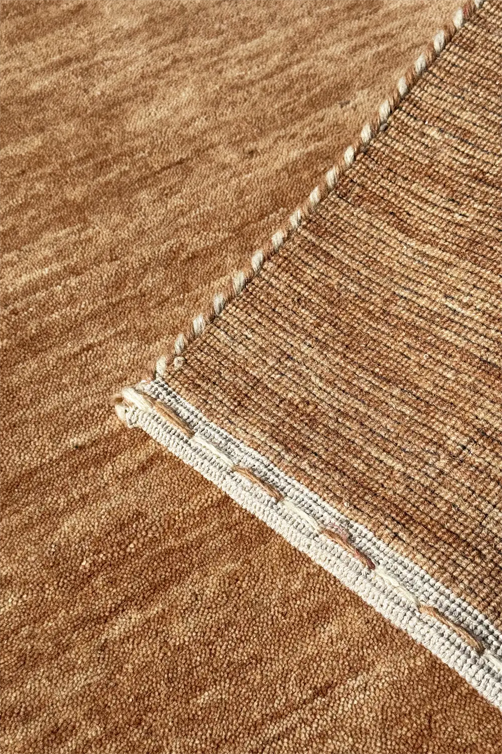 Close-up of a textured brown loomed rug with a visible stitching