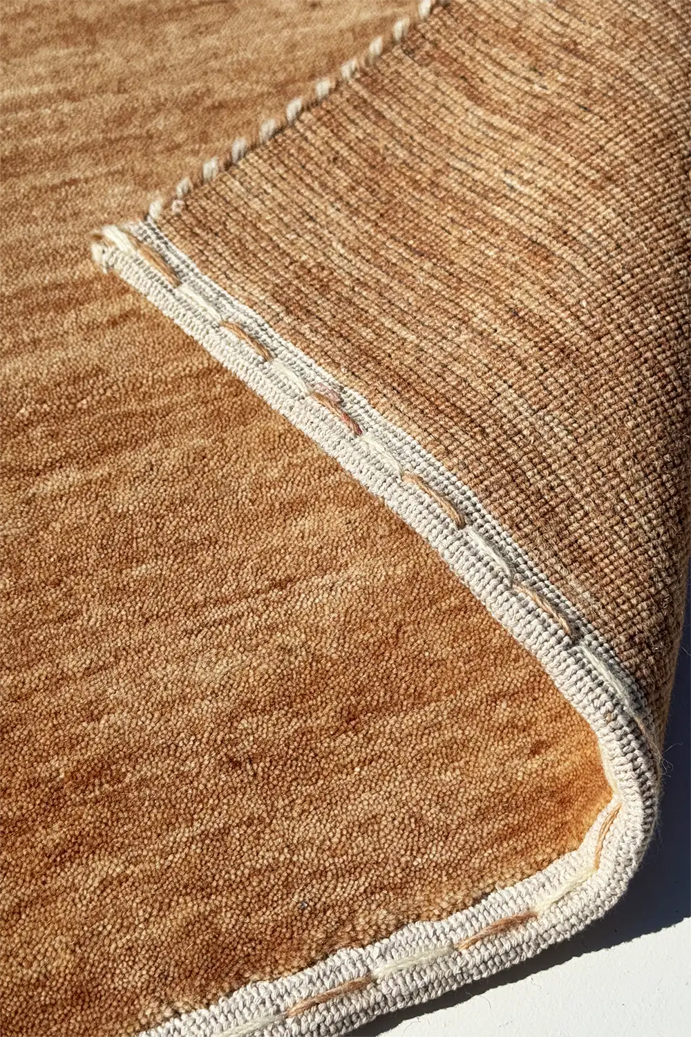 Close-up of a light warm brown textured wool area rug with a white border