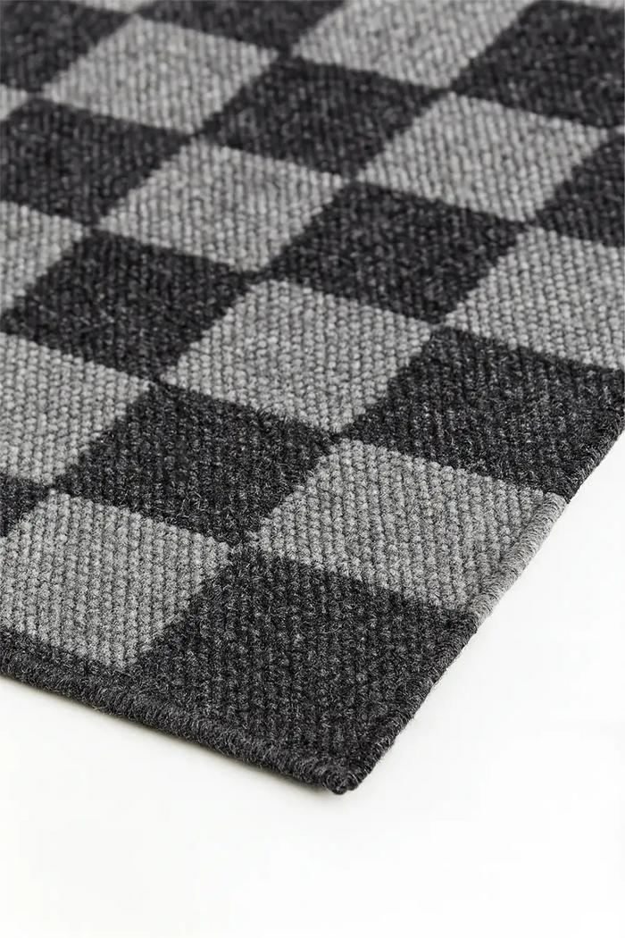 Close-up of a checkered black and gray woven wool rug on a white surface