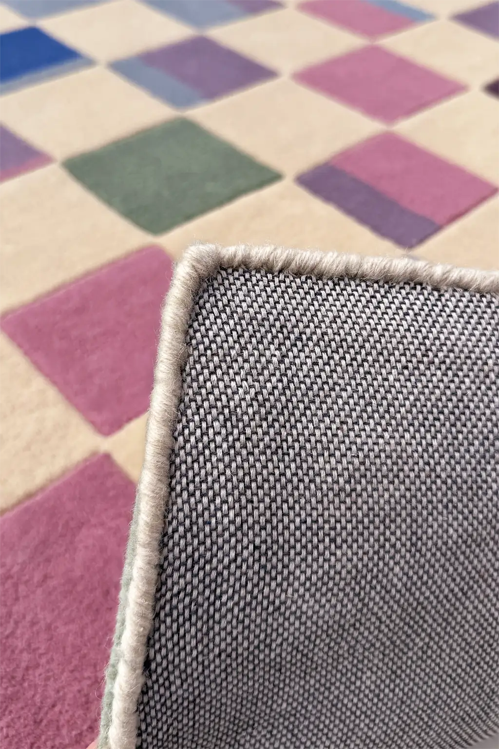Close-up of a textured white border on a checkered multicolored rug
