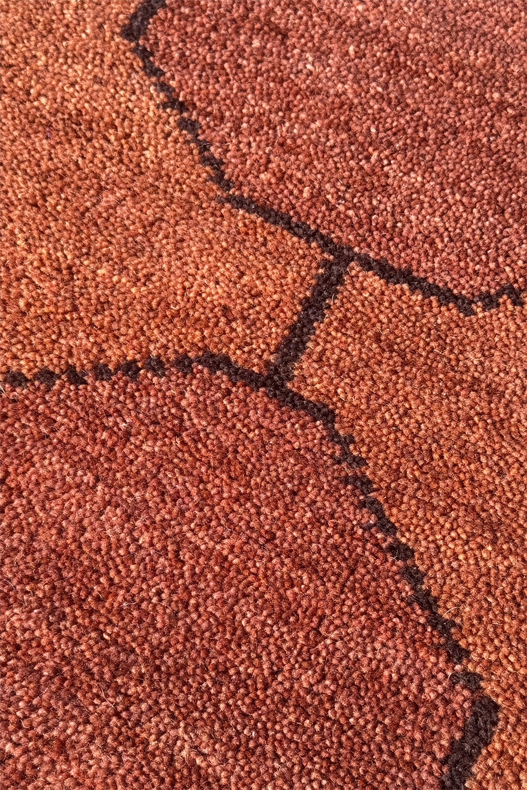 Close-up of a brown hand-knotted rug textured surface with black stitching