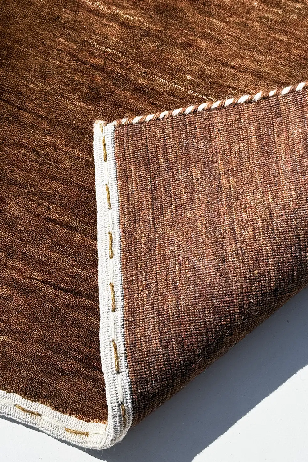 Close-up of a dark brown textured rug with a white border on a light gray background