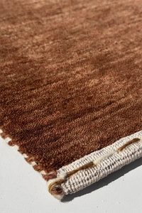 Close-up of a warm neutral brown textured wool rug corner on a light gray background chestnut