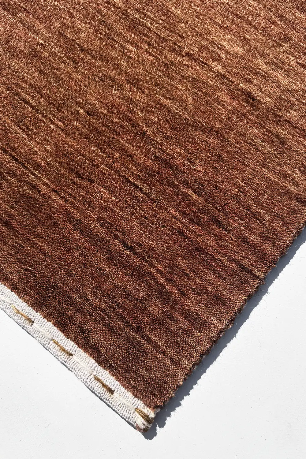 Close-up of a brown textured modern rug corner on a white background chestnut