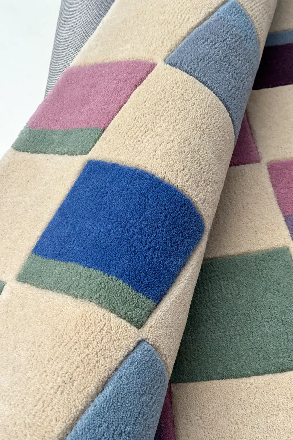 Close-up of a textured wool rug with geometric pattern in blue, green, and purple on a beige background.