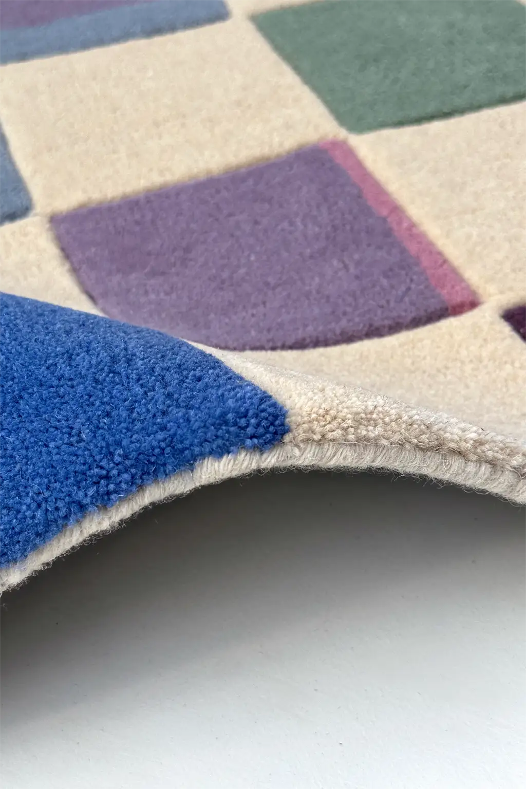 Close-up of a checkered runner rug with blue, purple, and beige squares on a white background.