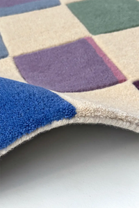 Close-up of a checkered runner rug with blue, purple, and beige squares on a white background.