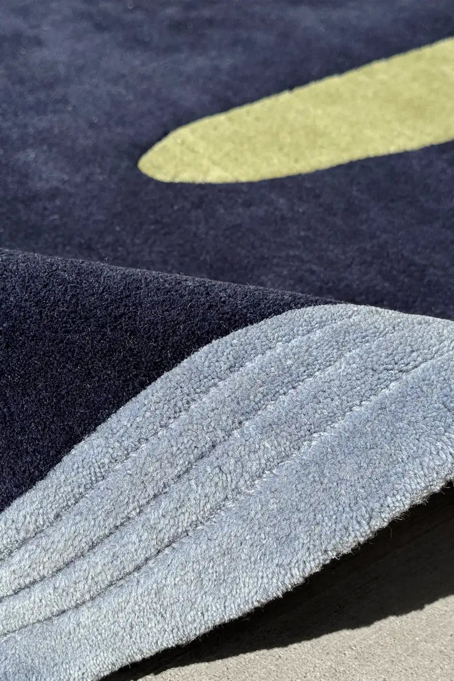 Close-up of abstract dark blue and sage green tufted wool rug with curved edges and bold graphic shapes