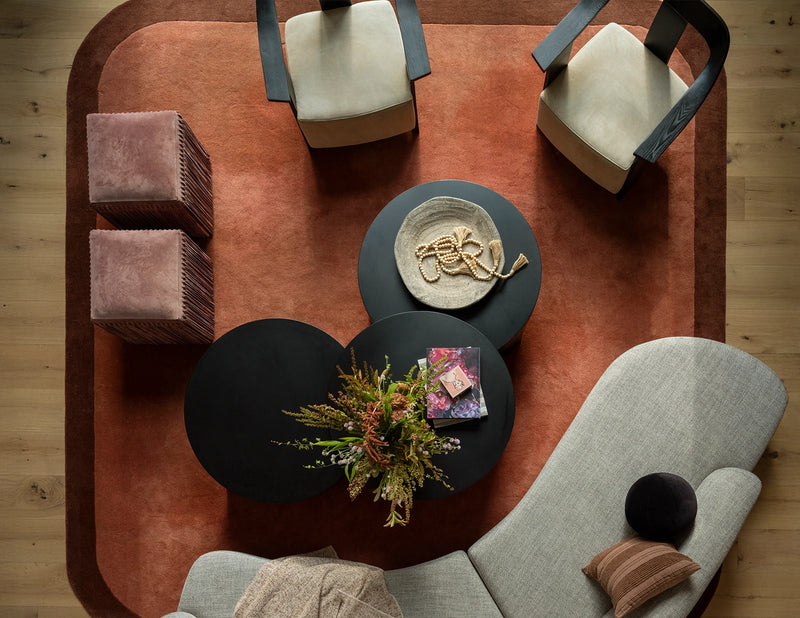 Modern living room with a brown rug, gray sofa, and decorative items on black coffee tables.