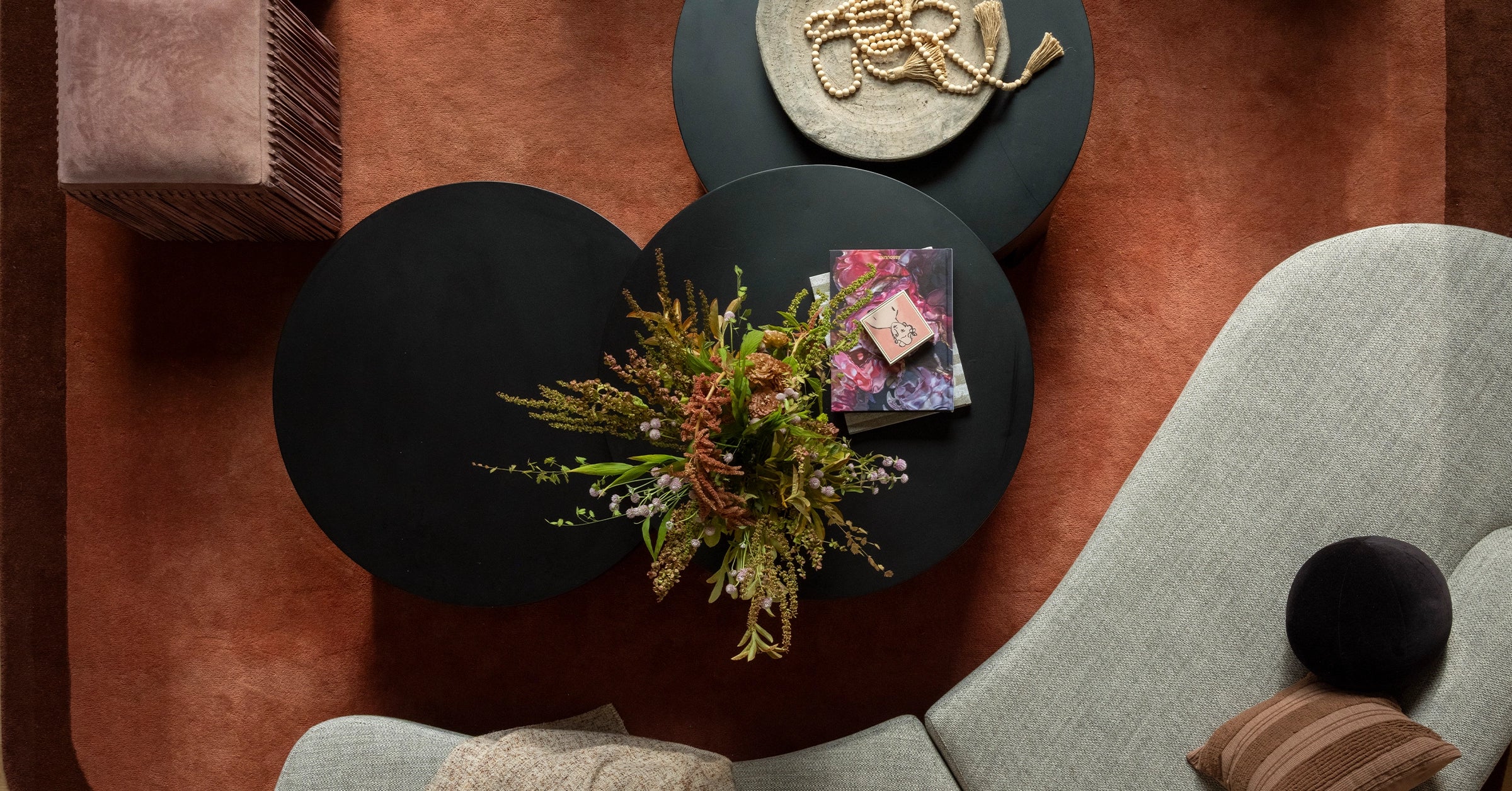 Modern living room with rust brown wool rug, round black coffee table, floral arrangement, and decorative items.