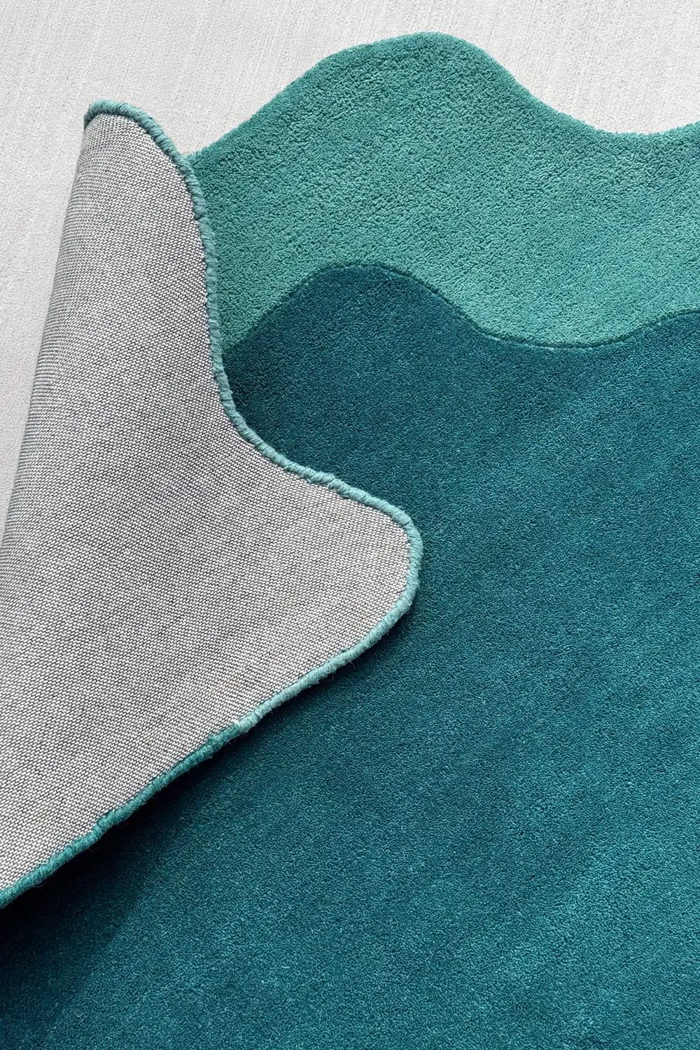 Rolled corner showing plush pile and wave edge of colorful teal and turquoise rug, great for bedrooms or odd-shaped spaces