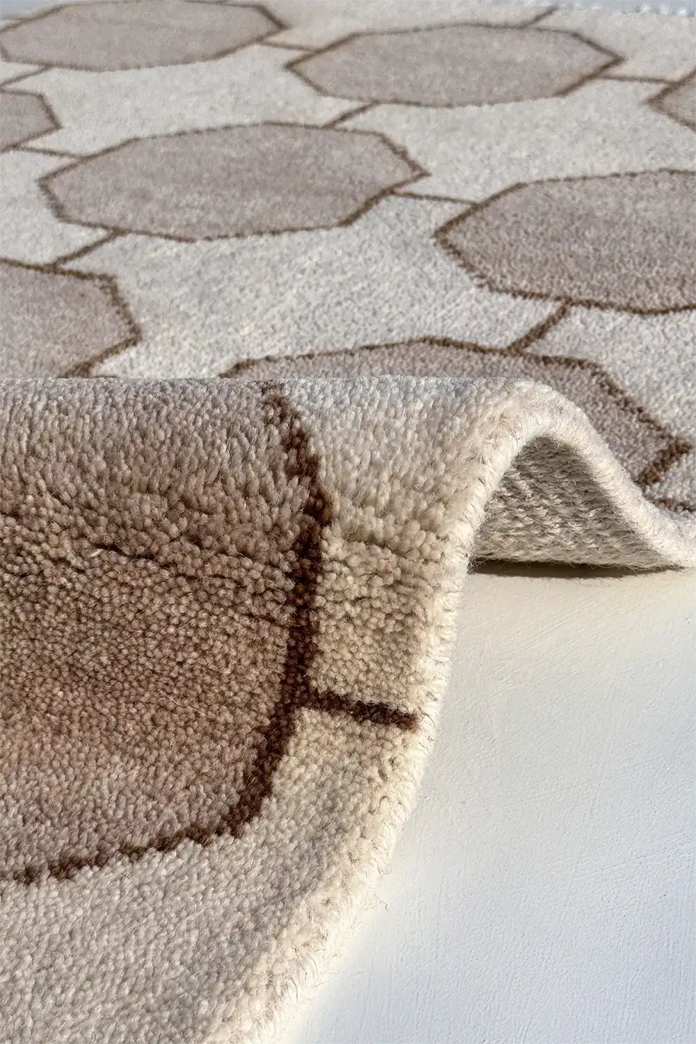 Close-up of a textured beige rug hand-knotted in wool with geometric pattern on a white background