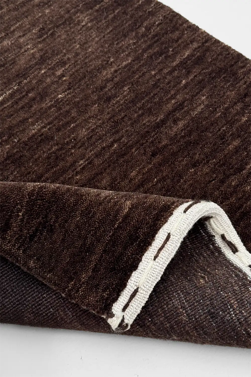 Close-up of a chocolate brown textured rug with a white border on a light gray background