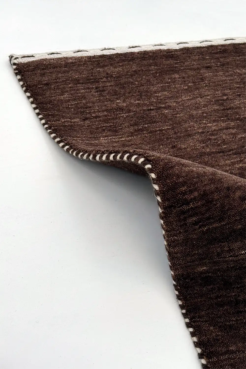 moody brown textured wool rug with a white border on a white background