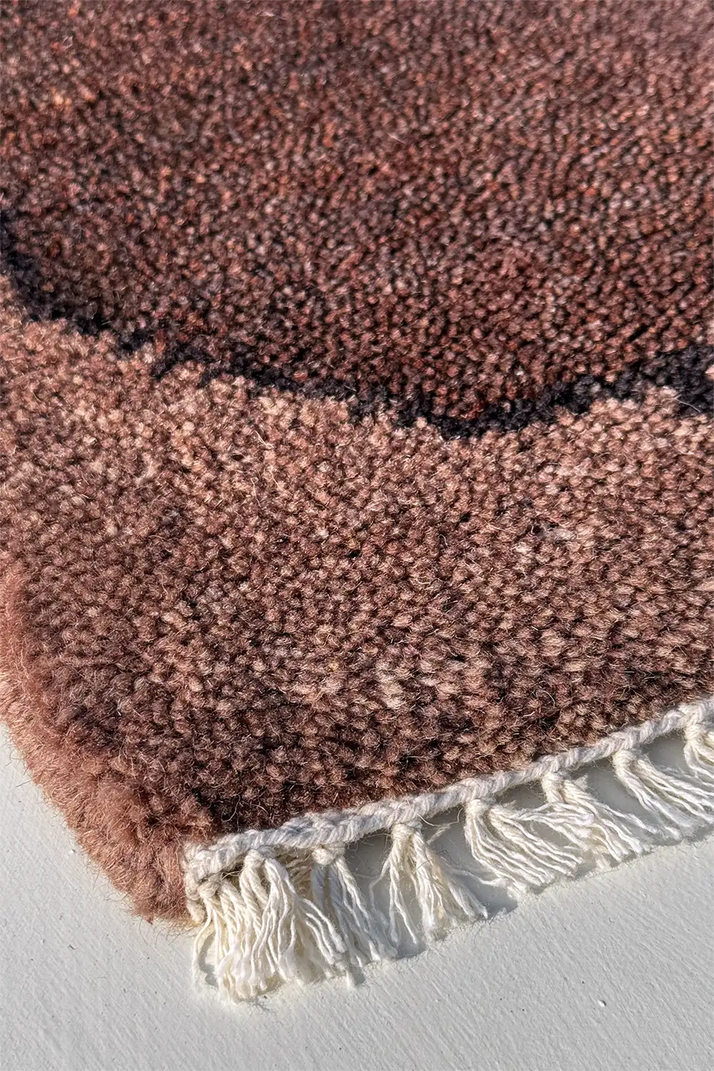chocolate brown textured rug with white fringe on a light gray background