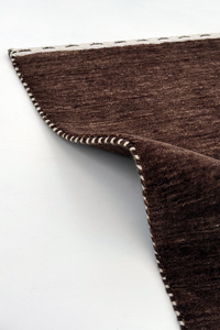 A close-up of a dark brown texture runner rug with a white whipstitched edge, folded over to show the underside and stitching detail against a plain white background cocoa