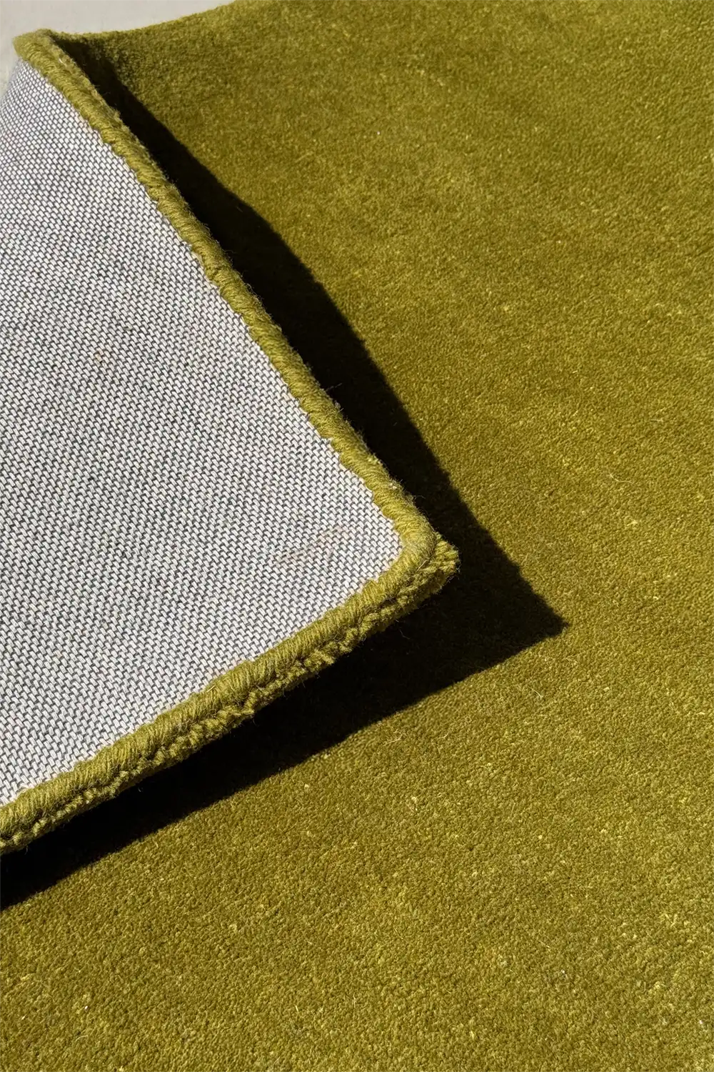 Close-up of a green square wool rug with a textured border